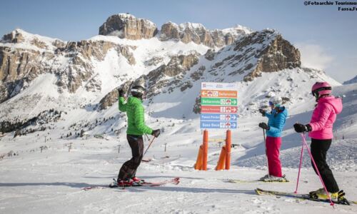 Skivergnügen in den Dolomiten Eine Gruppe von Skifahrern auf einer Skireise mit Single Aktiv Reisen fährt bei Sonnenschein durch die verschneiten Hänge der Dolomiten.